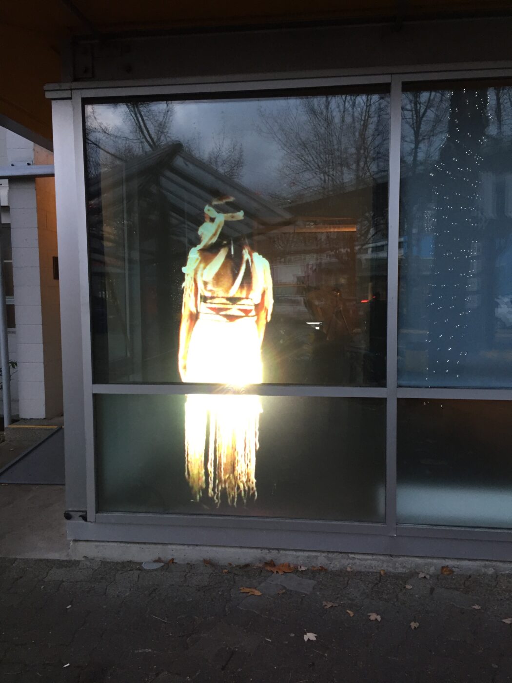 A projected image of ab Indigenous woman, turned away on a large window